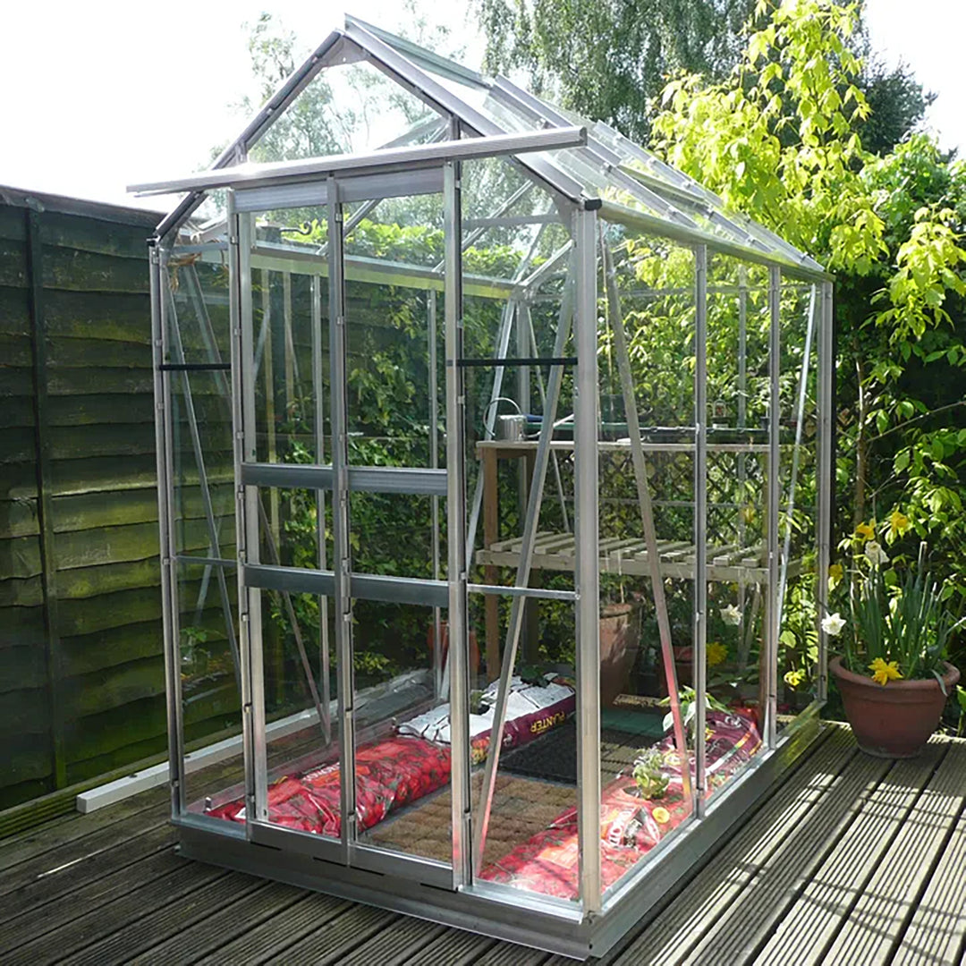 Cottage 6 greenhouse in aluminum finish, shown on a wood deck with internal staging and garden soil bags