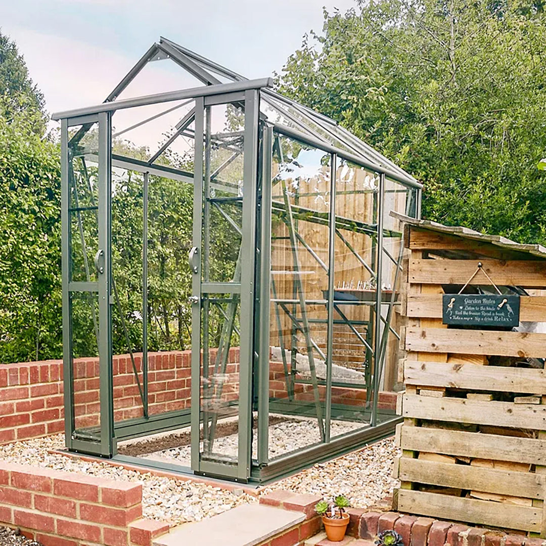 Cottage 6 greenhouse in graphite finish installed in a raised brick bed beside a rustic garden shed