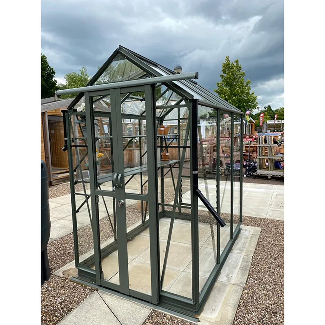 Cottage 6 greenhouse in graphite finish displayed in a garden center with open door and paved base