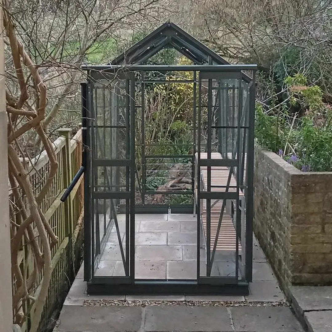Front view of Cottage 8 greenhouse in graphite finish, situated between fence and wall on a tile base